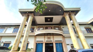 A grand entrance with large columns, a balcony, and a car parked in front. - Zahira Guesthouse Syariah (Jambi)