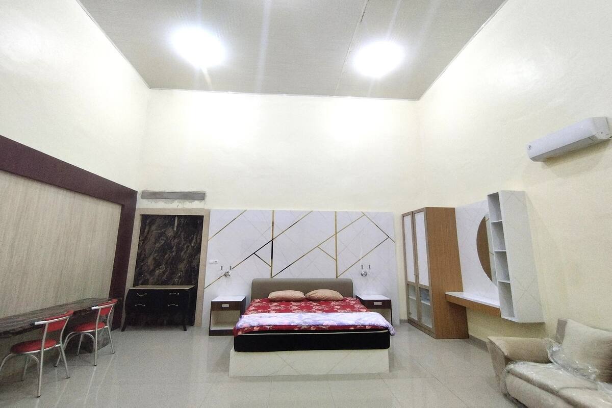Un dormitorio con cama, mesitas de noche, escritorio con sillas, sofá y estanterías empotradas.