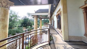 A balcony with a metal railing, a view of greenery, and a building with classical architecture. - Zahira Guesthouse Syariah (Jambi)