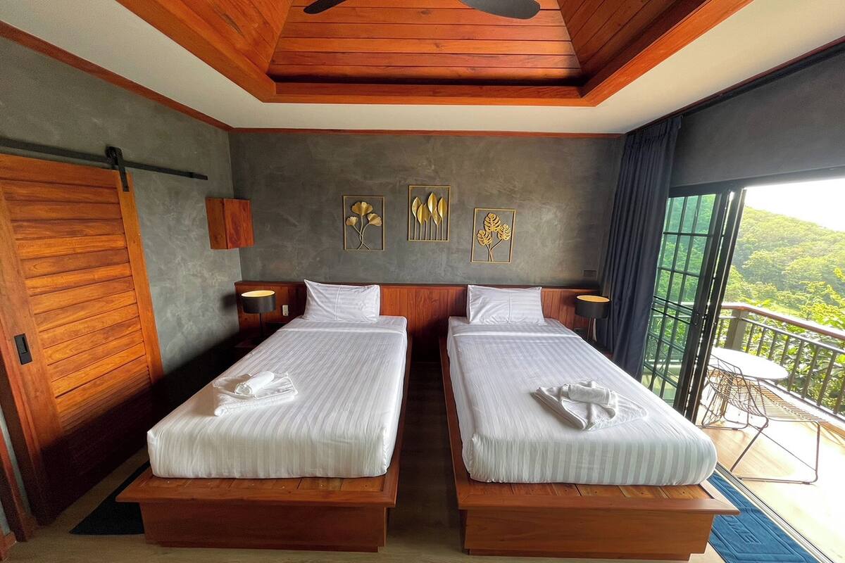 A room with two beds, wooden ceiling, and a balcony with a view.