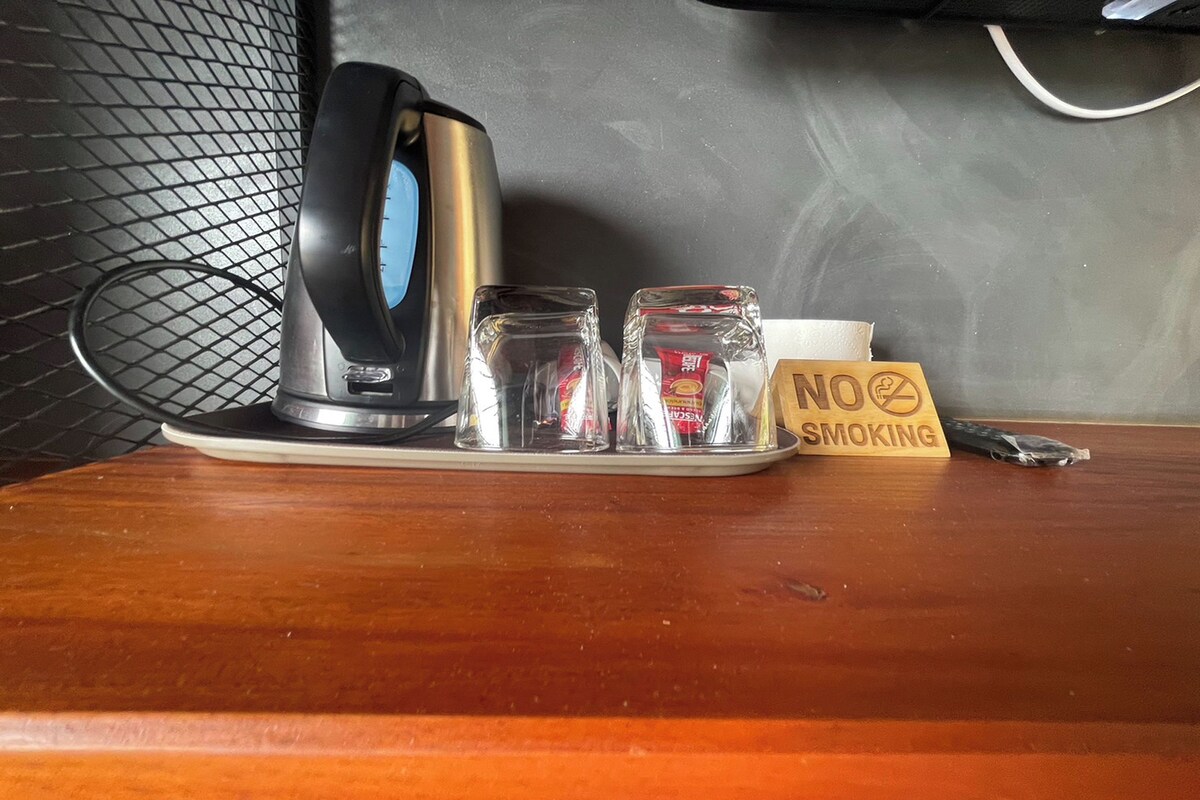 Una zona de cocina con un hervidor, dos recipientes de vidrio, un letrero de 'No Fumar' y un bolígrafo sobre una superficie de madera.