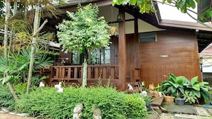 A traditional wooden house with a porch, surrounded by lush greenery and various potted plants. - Huen Pak Mon Chantra (Chiang Rai)
