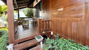 A wooden porch with a bench, a small statue, and a planter with green plants. - Huen Pak Mon Chantra (Chiang Rai)