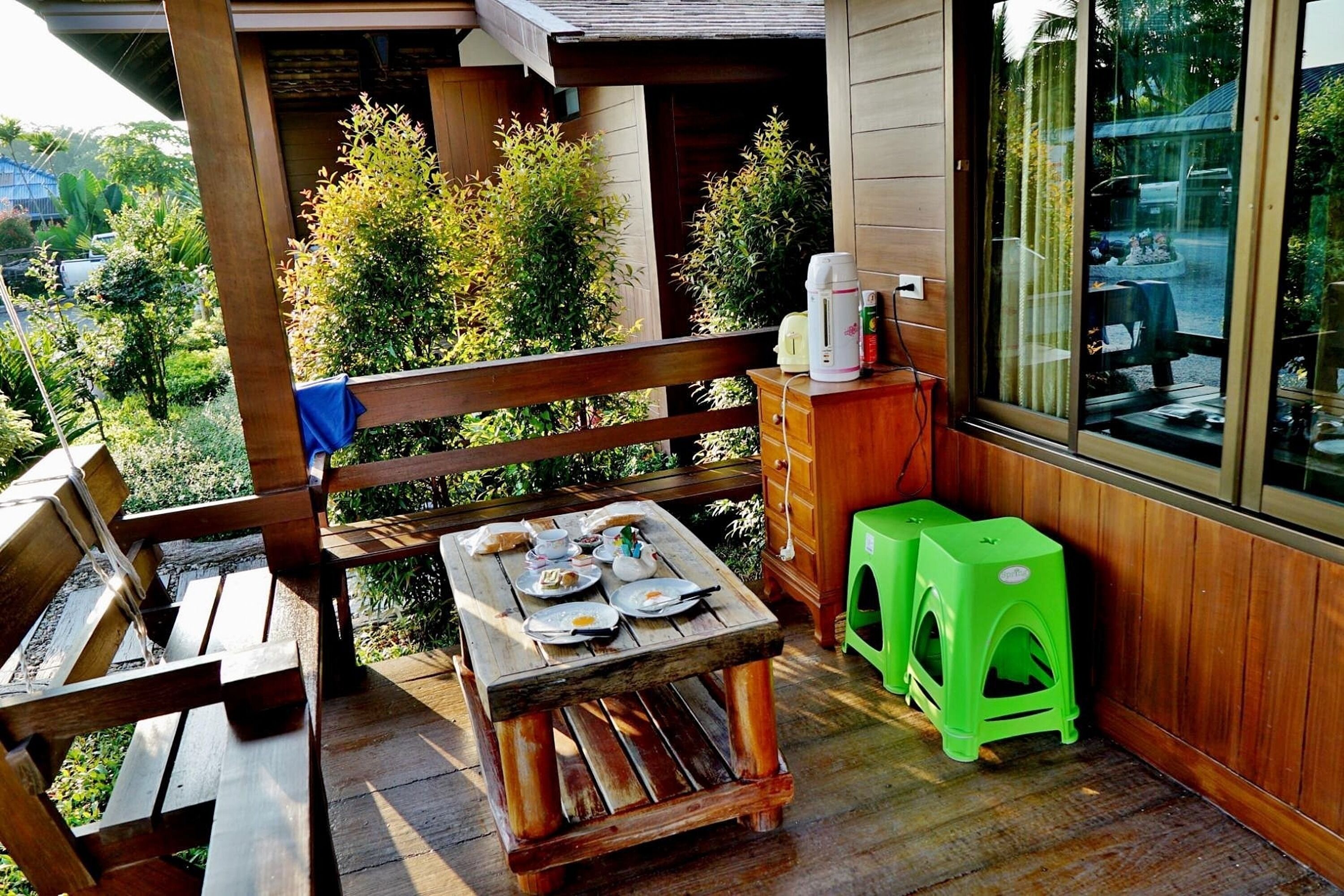 A wooden deck with a table set for a meal, a bench, and a green stool.