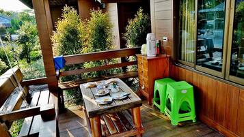A wooden deck with a table set for a meal, a bench, and a green stool.