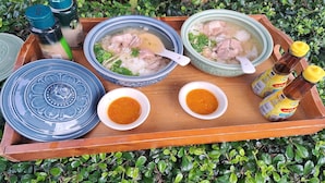 A tray with two bowls of soup, two small bowls of sauce, and condiment bottles. - Huen Pak Mon Chantra (Chiang Rai)