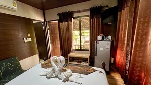 A hotel room with a neatly made bed, a small table with a chair, a refrigerator, and a window with curtains. - Huen Pak Mon Chantra (Chiang Rai)