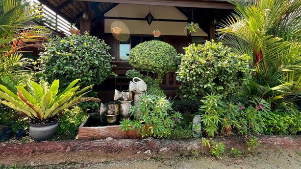 A wooden house with a covered porch, surrounded by various potted plants and greenery. - Huen Pak Mon Chantra (Chiang Rai)