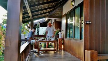 A wooden deck with a table and chairs, a wooden railing, and a view of the surrounding greenery.