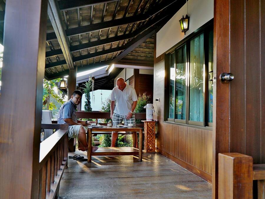 A wooden deck with a table and chairs, a wooden railing, and a view of the surrounding greenery.