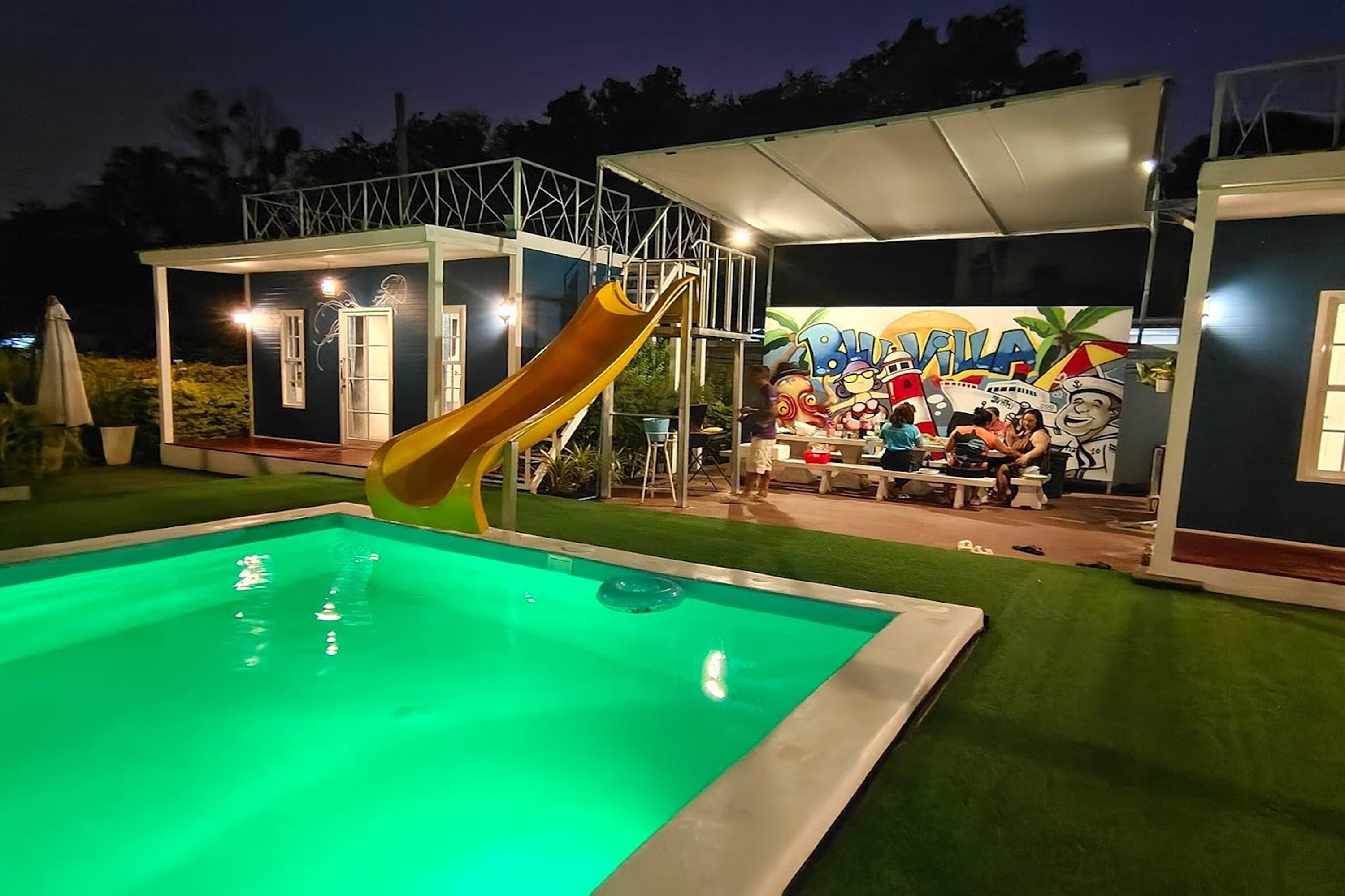 Una piscina con tobogán, un área de descanso cubierta y un mural con personajes de caricaturas.