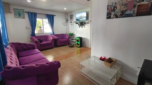 A living room with purple sofas, a TV mounted on the wall, and a cityscape painting. - Bluvilla Sattahip (Sattahip)