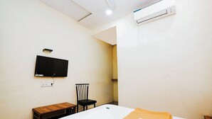 Una habitación pequeña y sencilla con una cama, una silla, una mesita, un televisor y aire acondicionado.