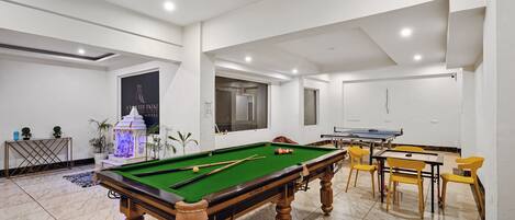 A pool table with yellow chairs, a ping pong table, and a billiards rack.