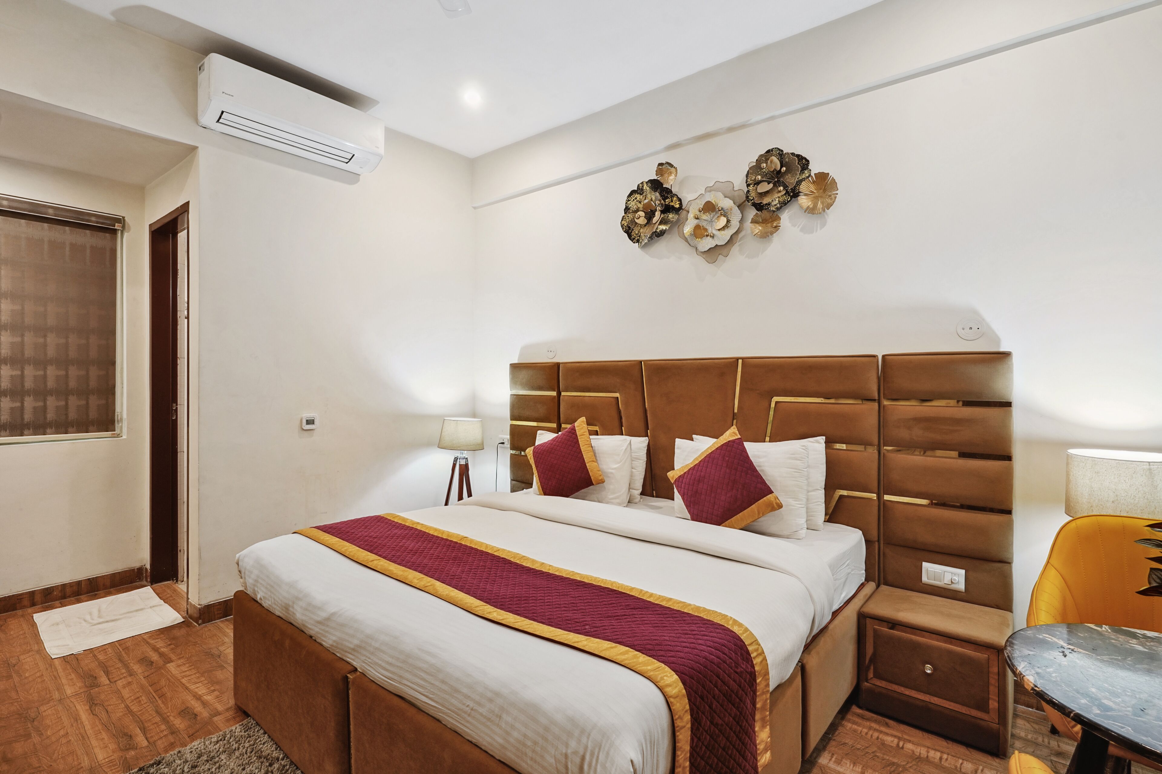 A hotel room with a large bed, a nightstand, a chair, and a wall-mounted air conditioner.