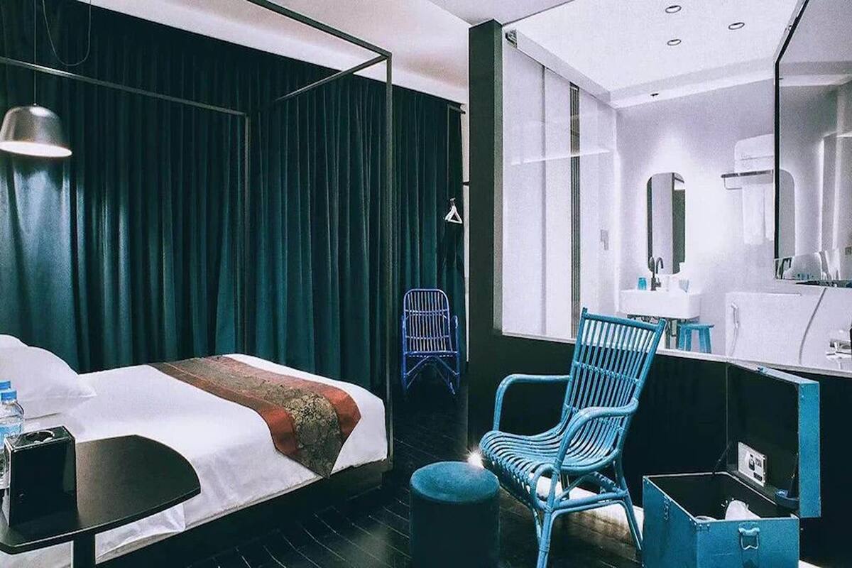 Une chambre d’hôtel moderne avec un grand lit, une chaise bleue, une petite table et un miroir.