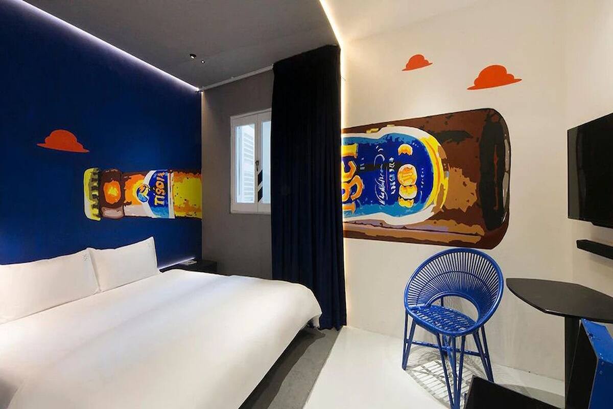 Une chambre d’hôtel avec un grand lit, une chaise bleue, une petite table et une fresque murale.