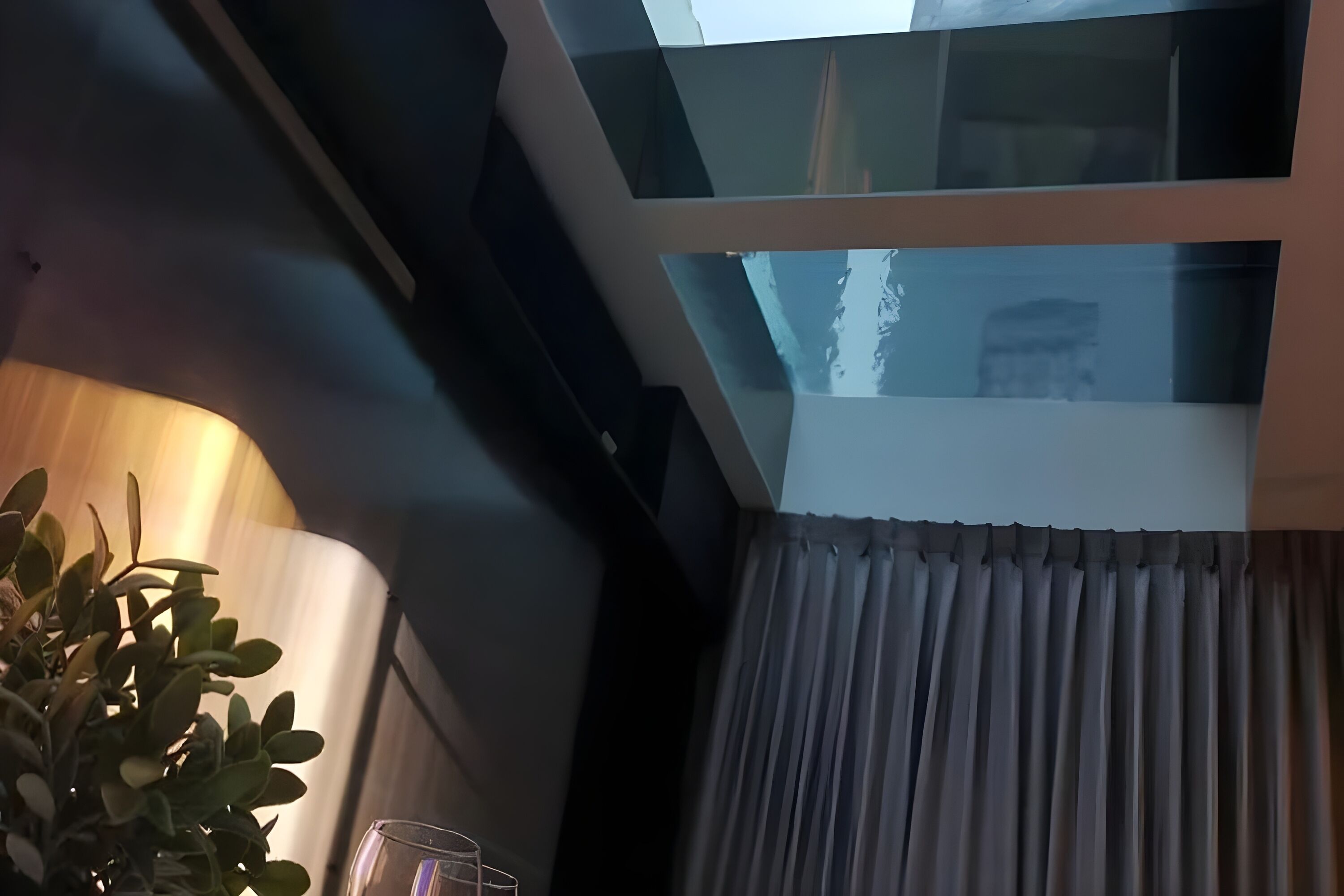 Ein modernes Interieur mit Glasdecke, einer Topfpflanze und einem mit Vorhängen versehenen Fenster.