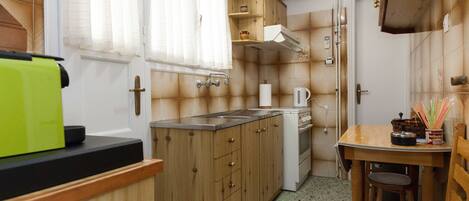 Una cocina compacta con armarios de madera, una pequeña encimera y una zona de comedor con mesa y silla de madera.