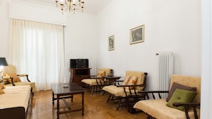 Ein Wohnzimmer mit Holzboden, einer Chandelierleuchtre, einem Sofa, einem Tisch und einem Fernseher.