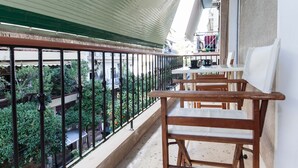 Ein Balkon mit Holzkubeln und einem Tisch, mit Blick auf einen Garten mit verschiedenen Pflanzen und einem Fahrrad im Hintergrund.