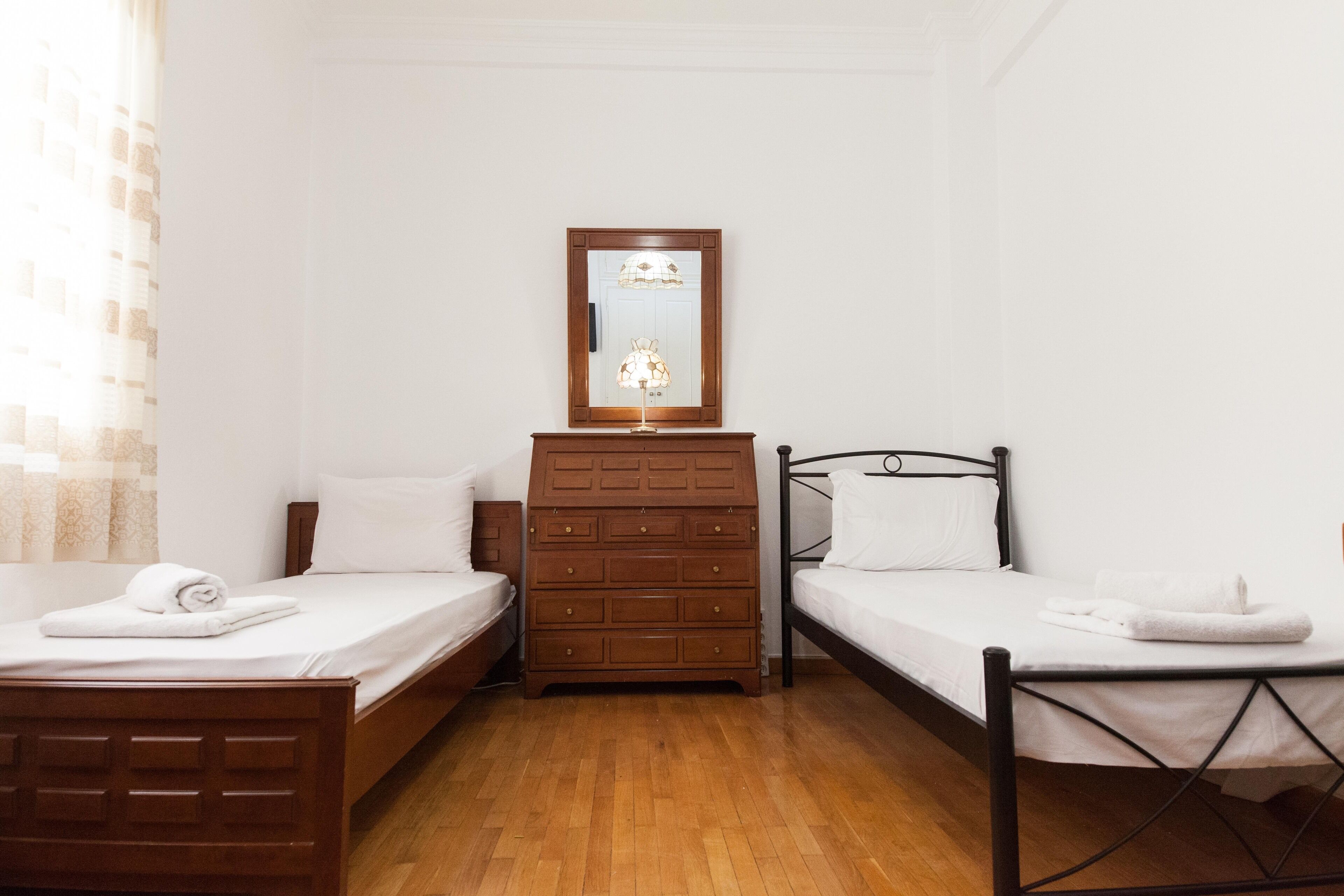 A hotel room with two single beds, a wooden dresser, a mirror, and a lamp.