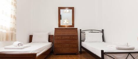 A hotel room with two single beds, a wooden dresser, a mirror, and a lamp.