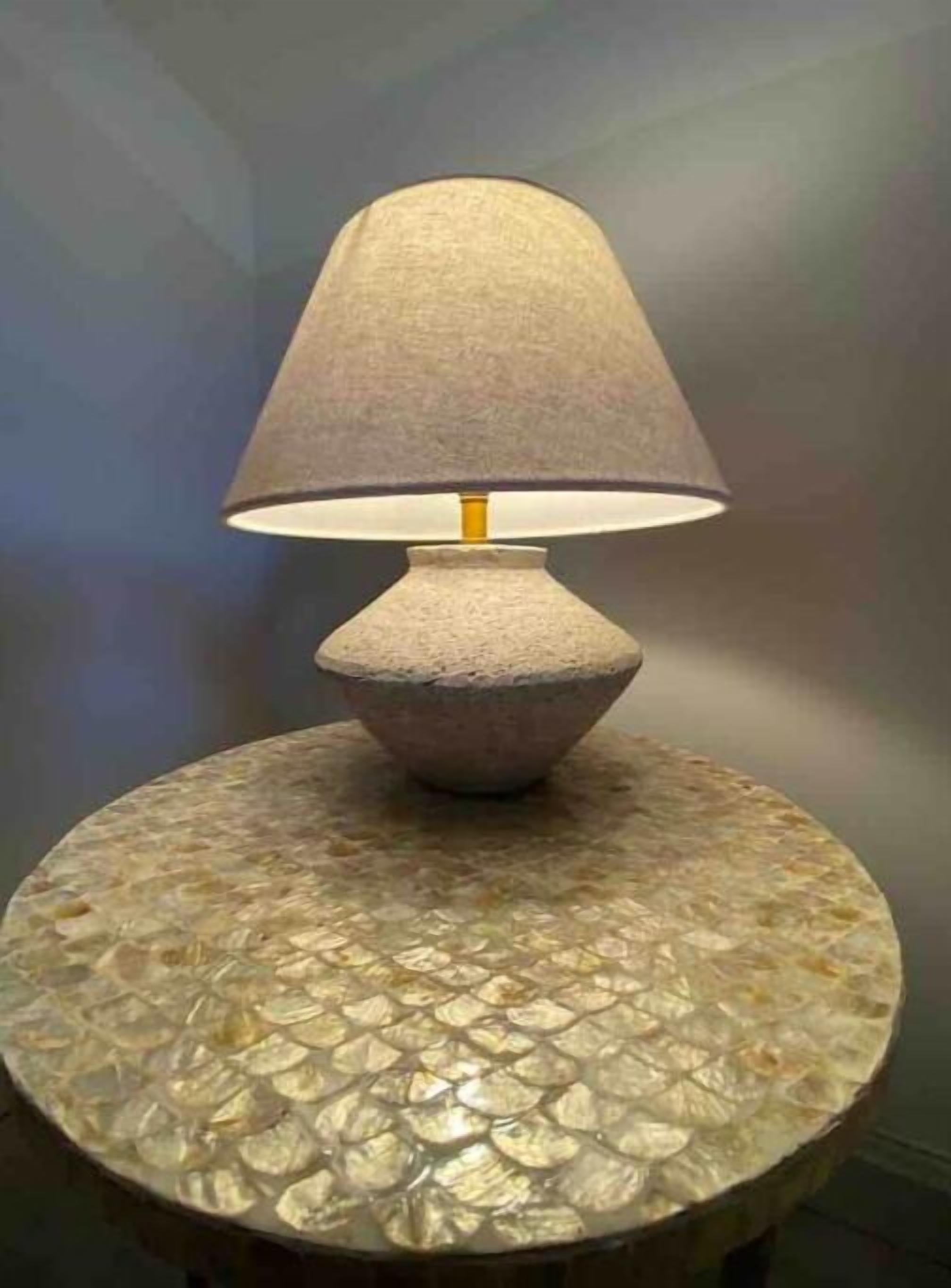 Une lampe dotée d’un abat-jour texturé, posée sur une table ronde dont le plateau présente un motif décoratif.