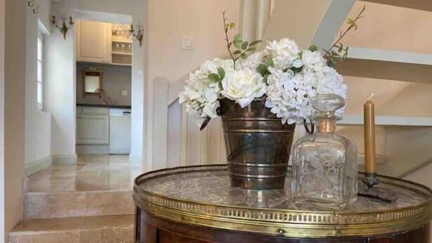 Ein runder Holztisch mit Marmorplatte, eine Metallvase mit weißen Blumen und eine Glasflasche.