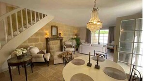 Ein geräumiges Wohnzimmer mit Treppe, einer Chandelieber und einem Essbereich mit Tisch und Stühlen.