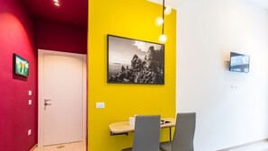 A room with a yellow accent wall, a framed black and white photograph, a flat-screen TV, and a table with two chairs. - Central Station Apartments & Suites by Wonderful Italy (Naples)
