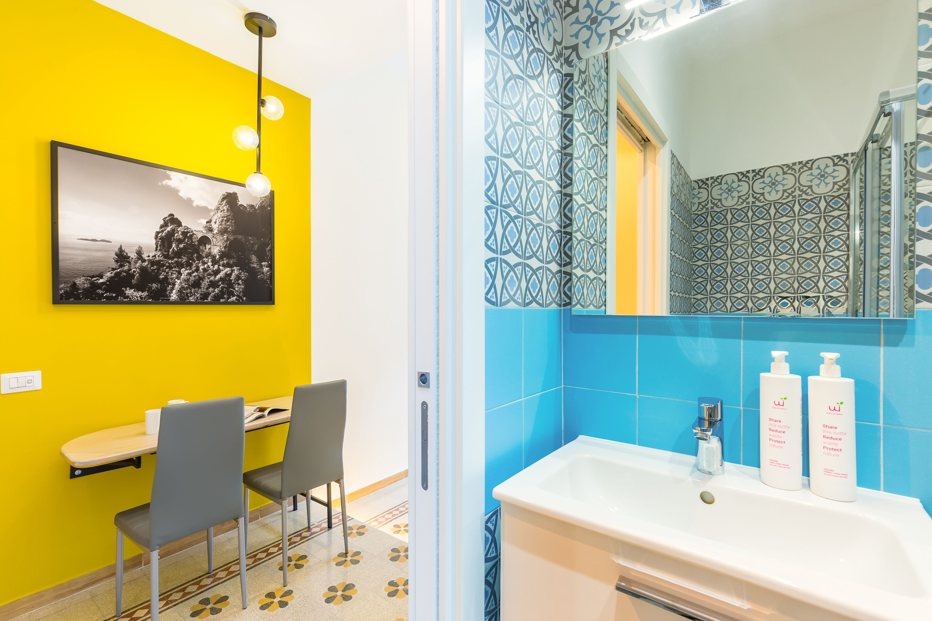 A bathroom with a white sink, blue tiles, and a mirror. There are two bottles of shampoo on the sink.