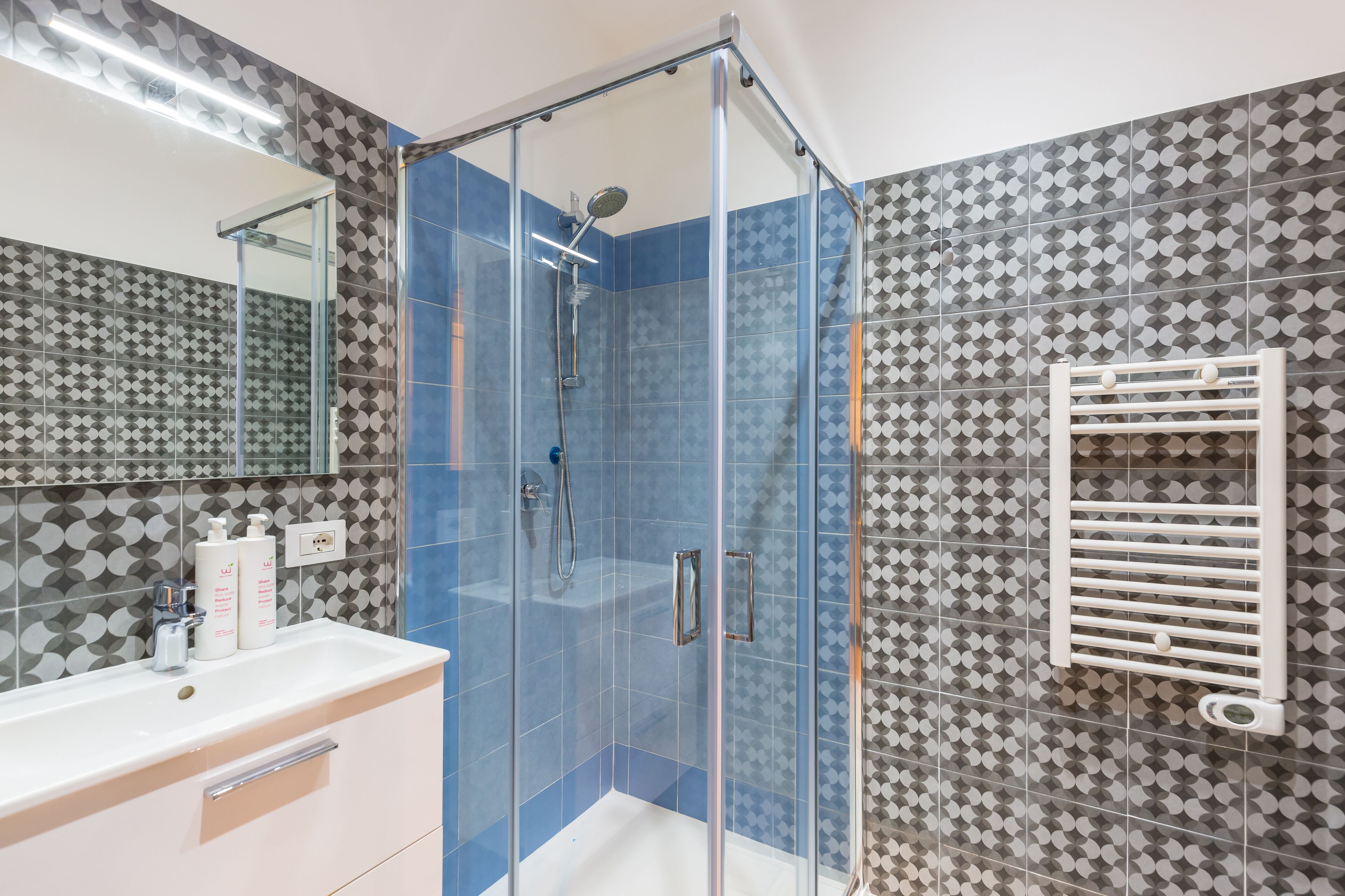 A bathroom with a glass-enclosed shower, a sink with a mirror, and patterned tiles.