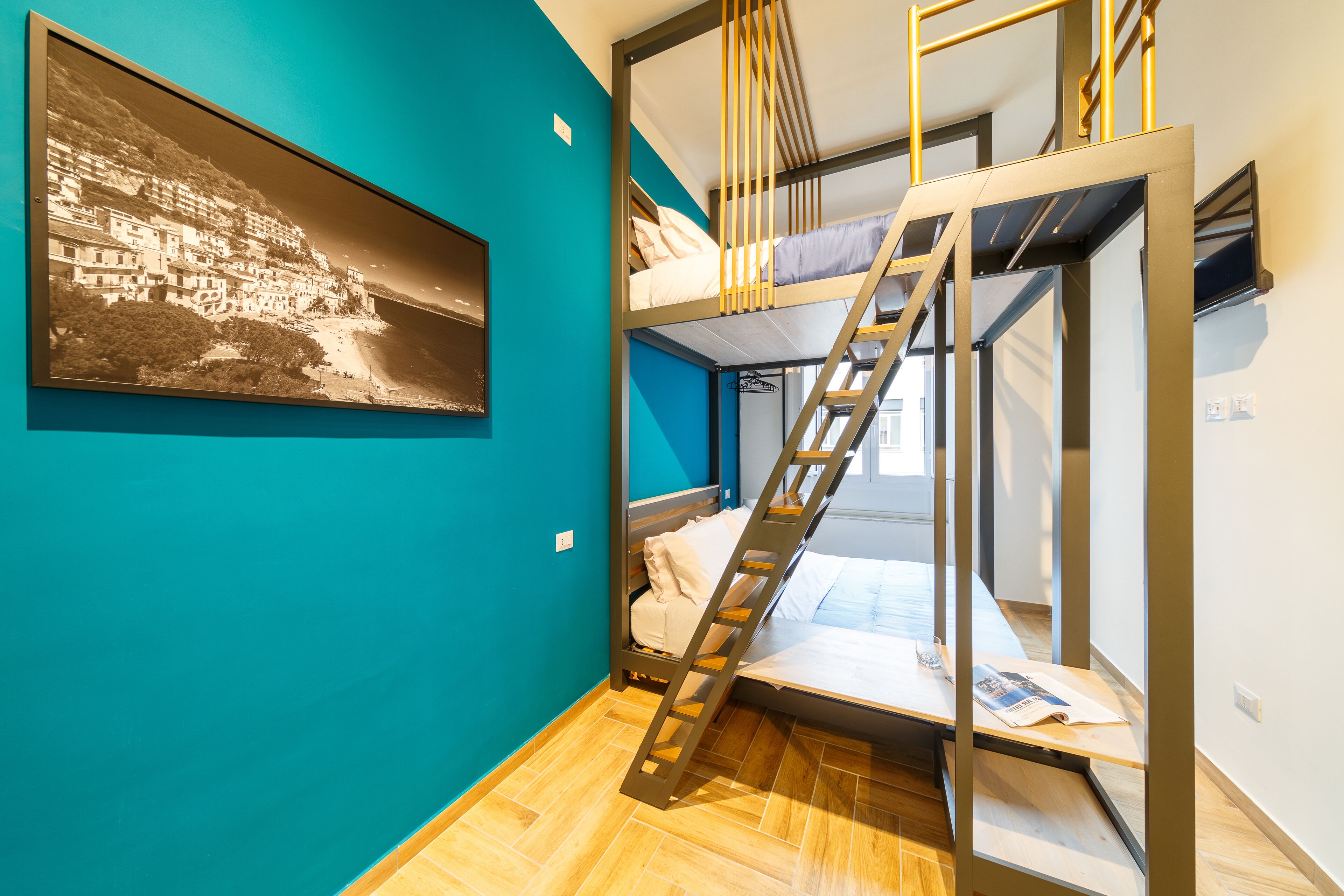 A room with a bunk bed, a ladder, and a framed black and white photograph on the wall.