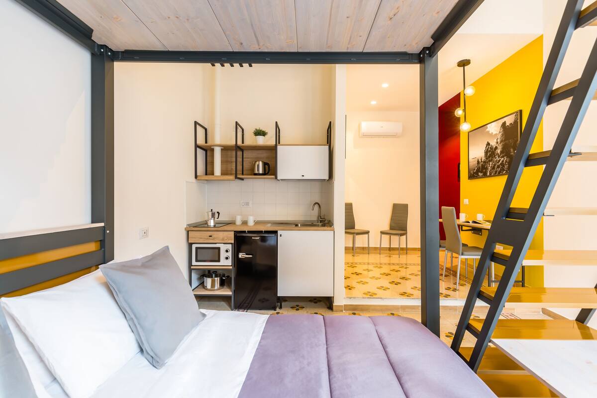 Quarto pequeno com cama, cozinha compacta e espaço para refeições.