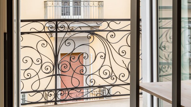 A view from a balcony with ornate metal railings, a window with a wooden shutter, and a building facade with decorative moldings. - Central Station Apartments & Suites by Wonderful Italy (Naples)