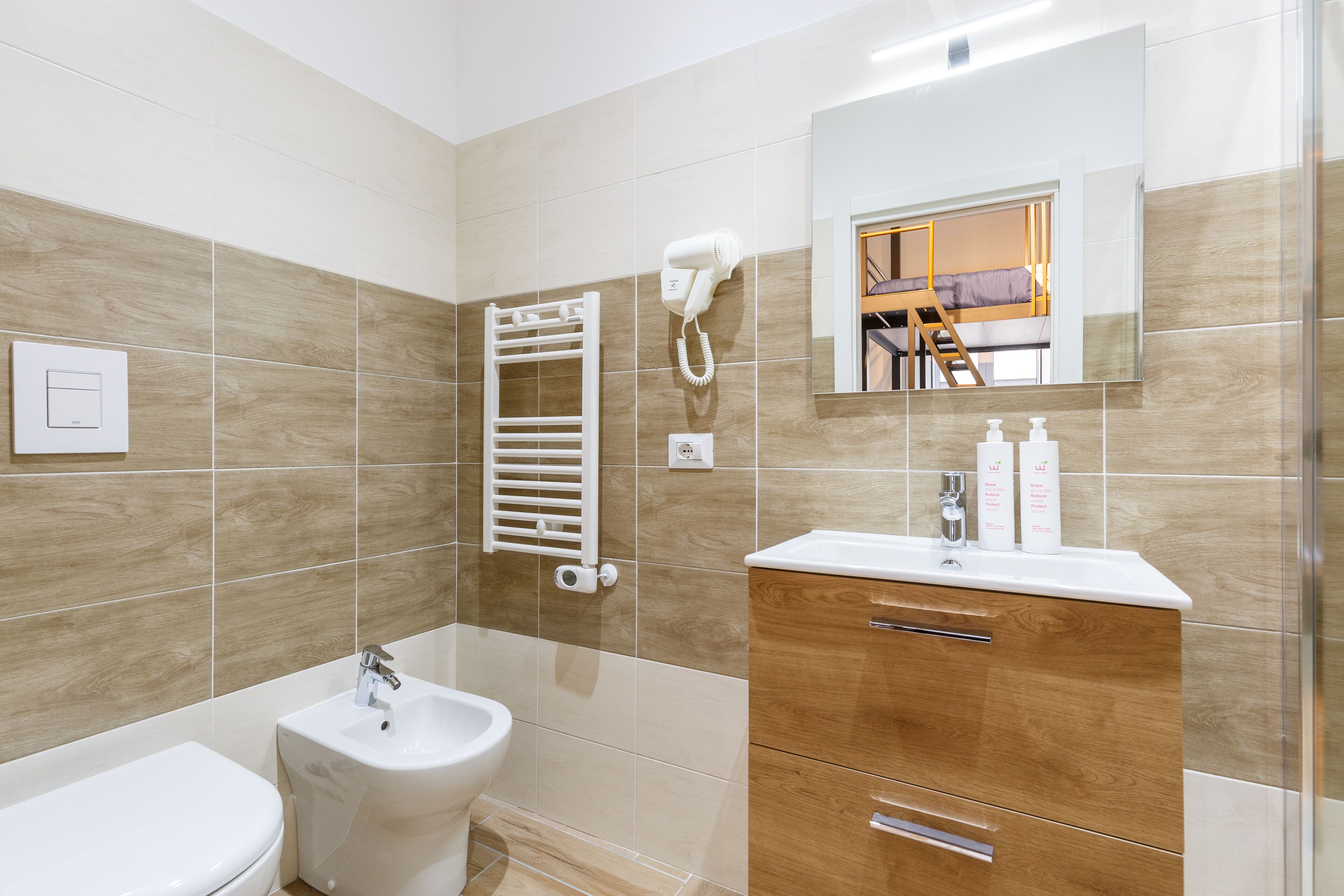 A modern bathroom with a toilet, bidet, vanity with a mirror, and a towel rack.