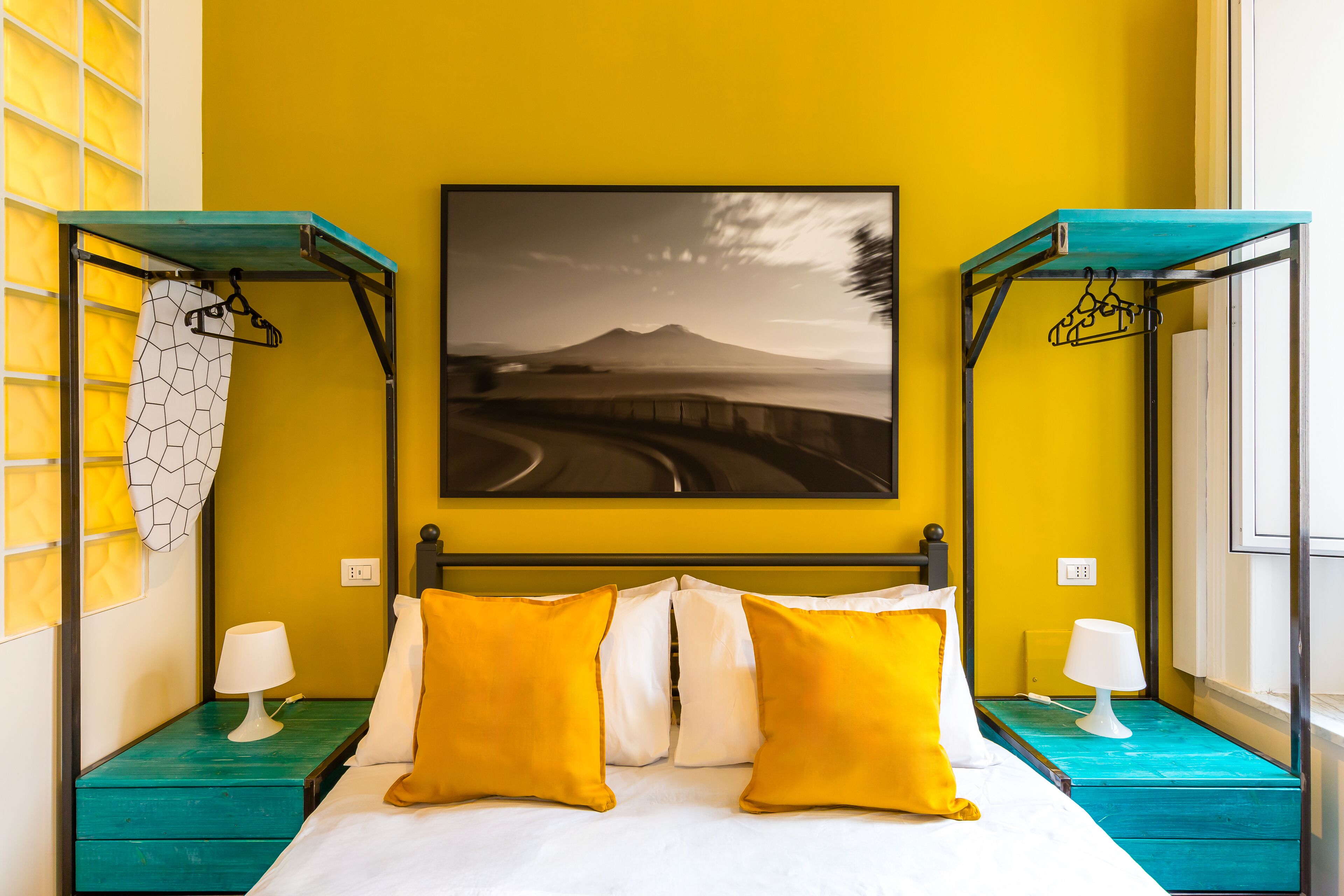 A hotel room with a bed, two nightstands, a painting of a landscape, and a window.