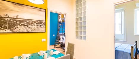 A dining area with a blue table set for four, a ladder leading to a blue door, and a bed with a blue bedspread in the adjacent room.