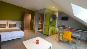 A modern hotel room with a bed, a dining table, and a kitchen area.