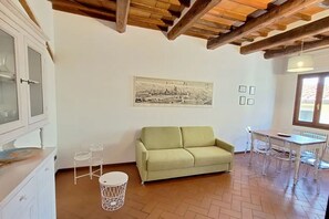 A room with a wooden ceiling, a green sofa, a dining table with chairs, a radiator, and a wall-mounted picture. - Casa Mojito, apartment in the Santa Croce district (Firenze)