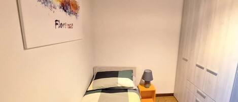 A bedroom with a bed, a nightstand, a lamp, a wardrobe, and a wall art piece.