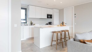 A modern kitchen with white cabinetry, a central island with stools, and a grey sofa in the living area. - SouthBay Luxury exclusive penthouse with incredible sea views and Estepona  (Estepona)