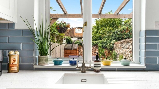 A kitchen with a window overlooking a garden, a sink, and various kitchen items on the windowsill. - Little Braybrooke Cottage- Saffron Walden (Saffron Walden)