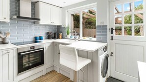 A compact kitchen with white cabinets, a built-in oven, a coffee machine, and a washing machine. - Little Braybrooke Cottage- Saffron Walden (Saffron Walden)