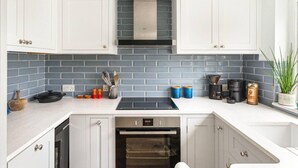 A modern kitchen with white cabinets, a stainless steel range hood, a built-in oven, and a blue-tiled backsplash. - Little Braybrooke Cottage- Saffron Walden (Saffron Walden)