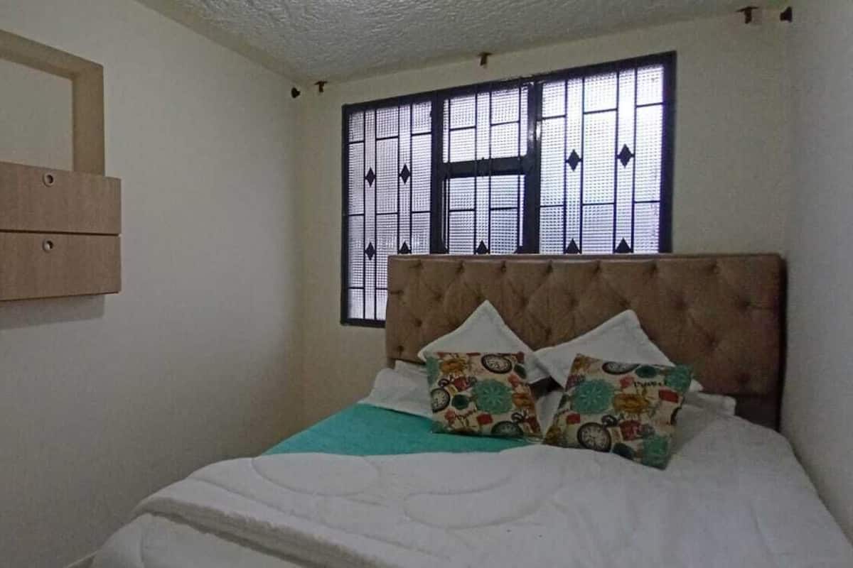 Une chambre à coucher avec un lit, une fenêtre munie d’un moustiquaire métallique et un tableau accroché au mur.