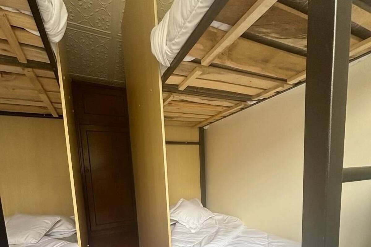 Un couloir étroit, avec des lits superposés de chaque côté, un plancher en bois et une porte au fond.