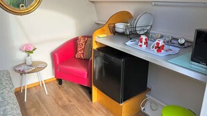Une cuisine compacte équipée d’un réfrigérateur, d’un évier et d’un petit coin repas avec une chaise rouge et un vase de fleurs.