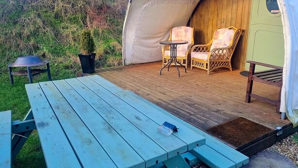 Un espace extérieur abrité comprenant une table de pique-nique, deux chaises en osier et une petite table.